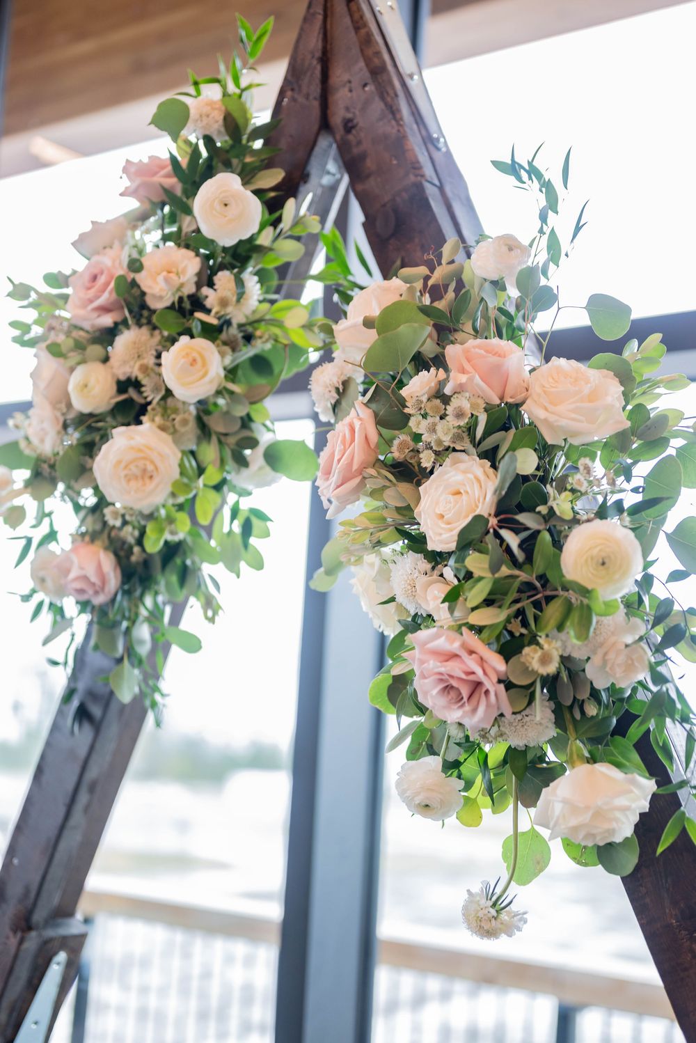 Elegant wedding floral arrangements of blush roses and greenery suspended from wooden triangular frames.