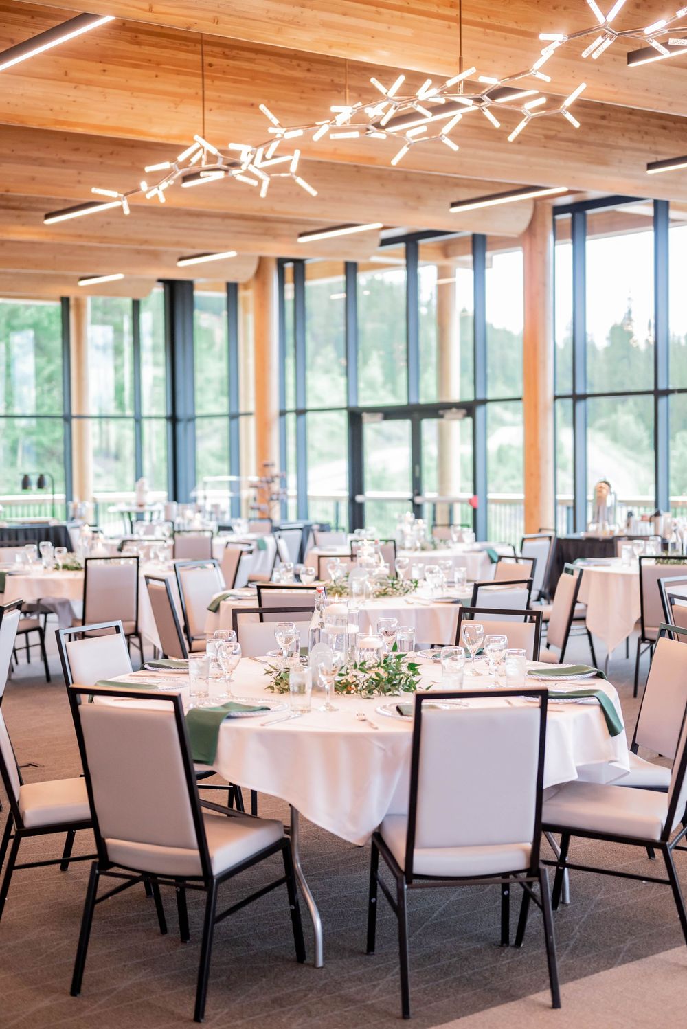 Modern event venue with round dining tables, white linens, upholstered chairs and artistic ceiling lighting fixtures.