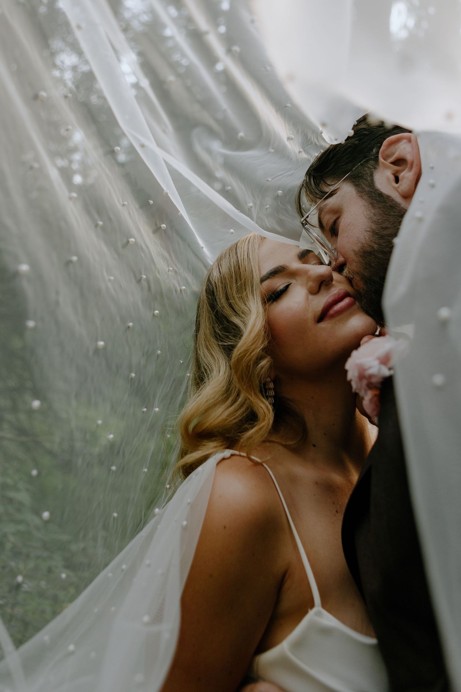 Romantic couple sharing an intimate moment under a sheer veil with dreamy bokeh light effects in the background.