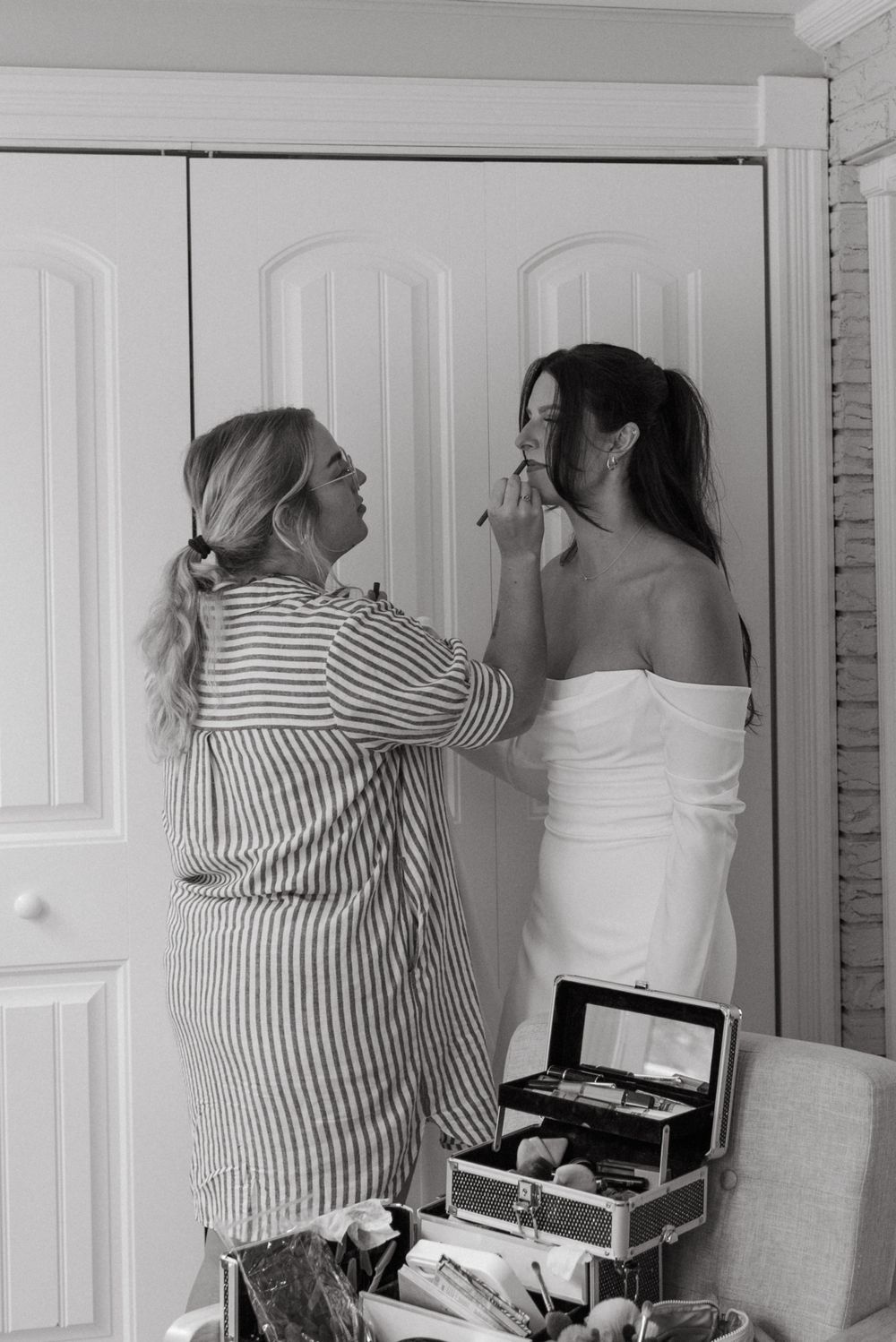 Black and white photo of final bridal preparations with someone in a striped dress helping adjust a white gown.