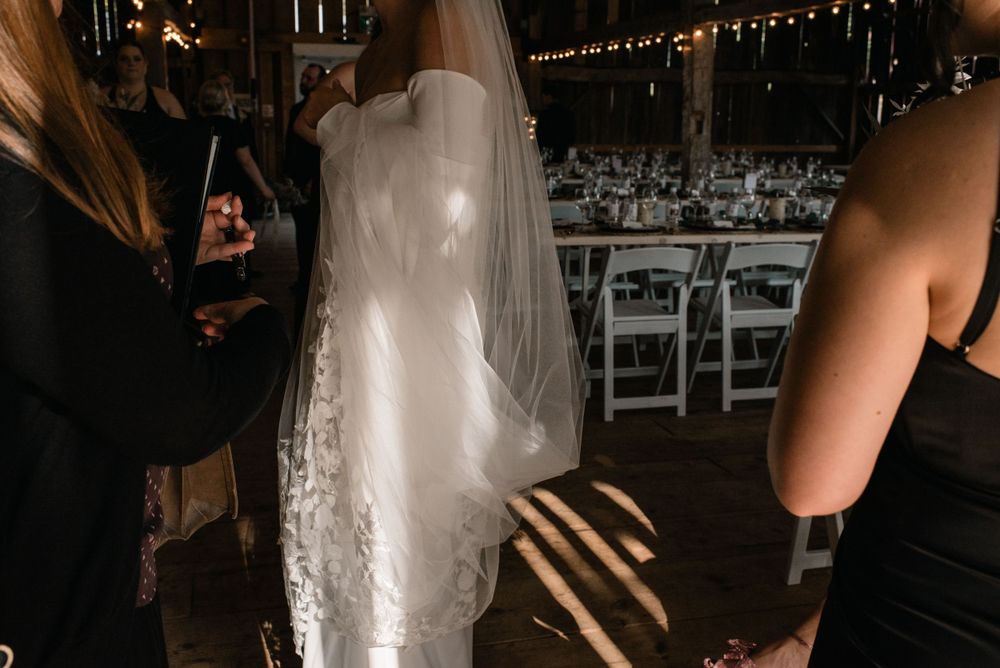 A flowing white wedding dress with delicate lace details is captured in motion at an indoor reception venue with string lights.