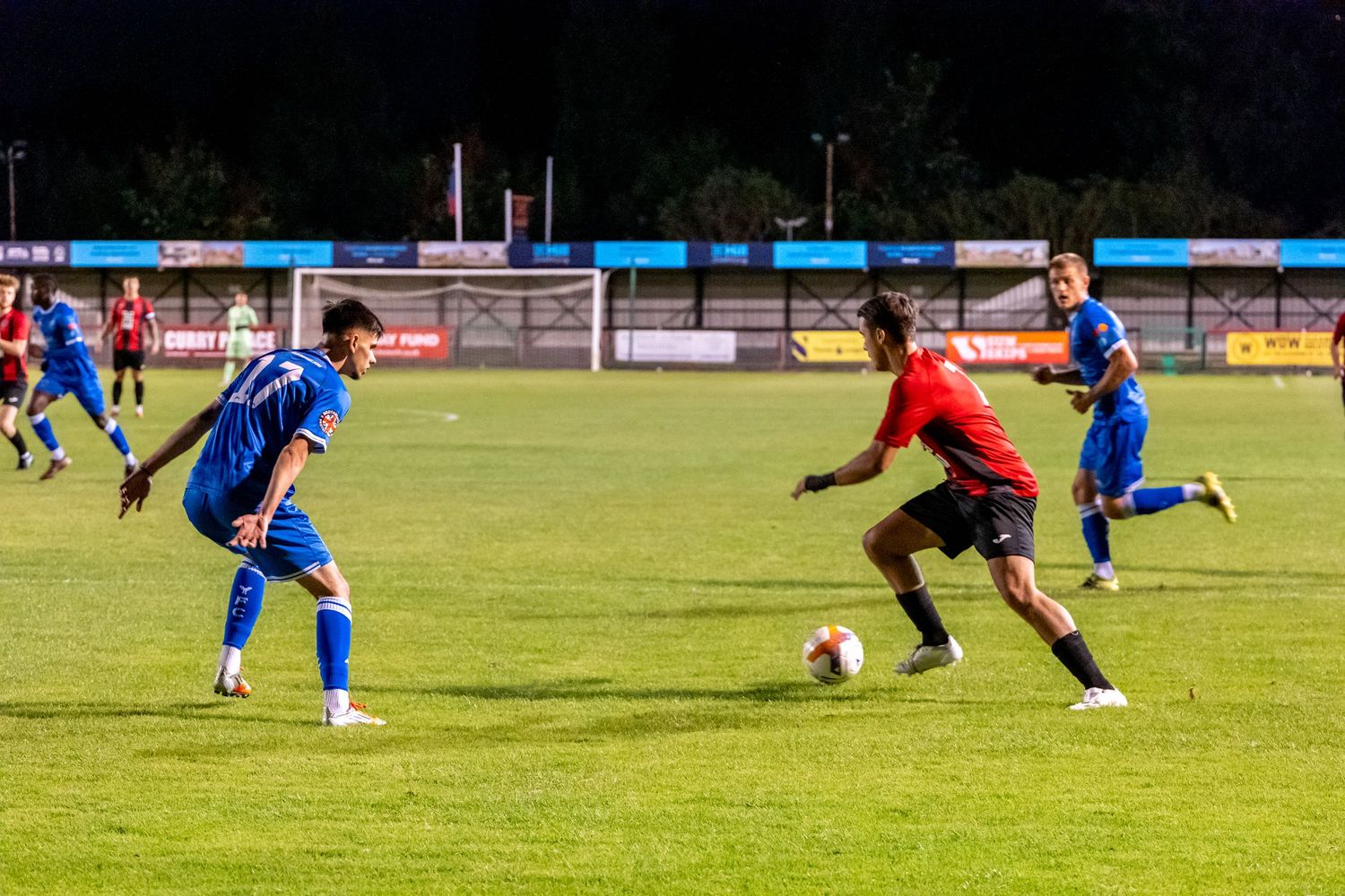 Soccer players battle for possession during a nighttime match under floodlights.
