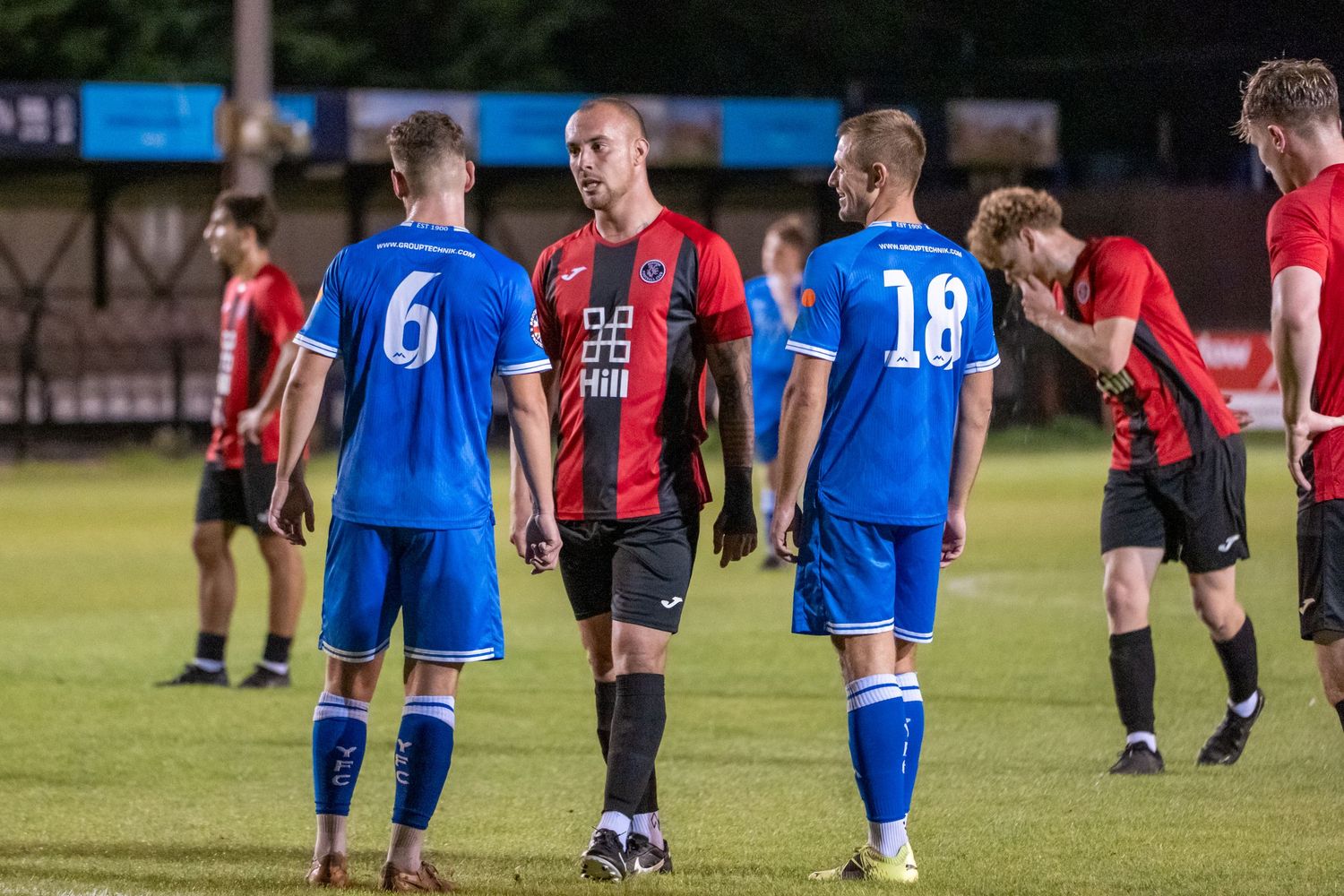 Players in blue and red-black striped jerseys interact during a soccer match.