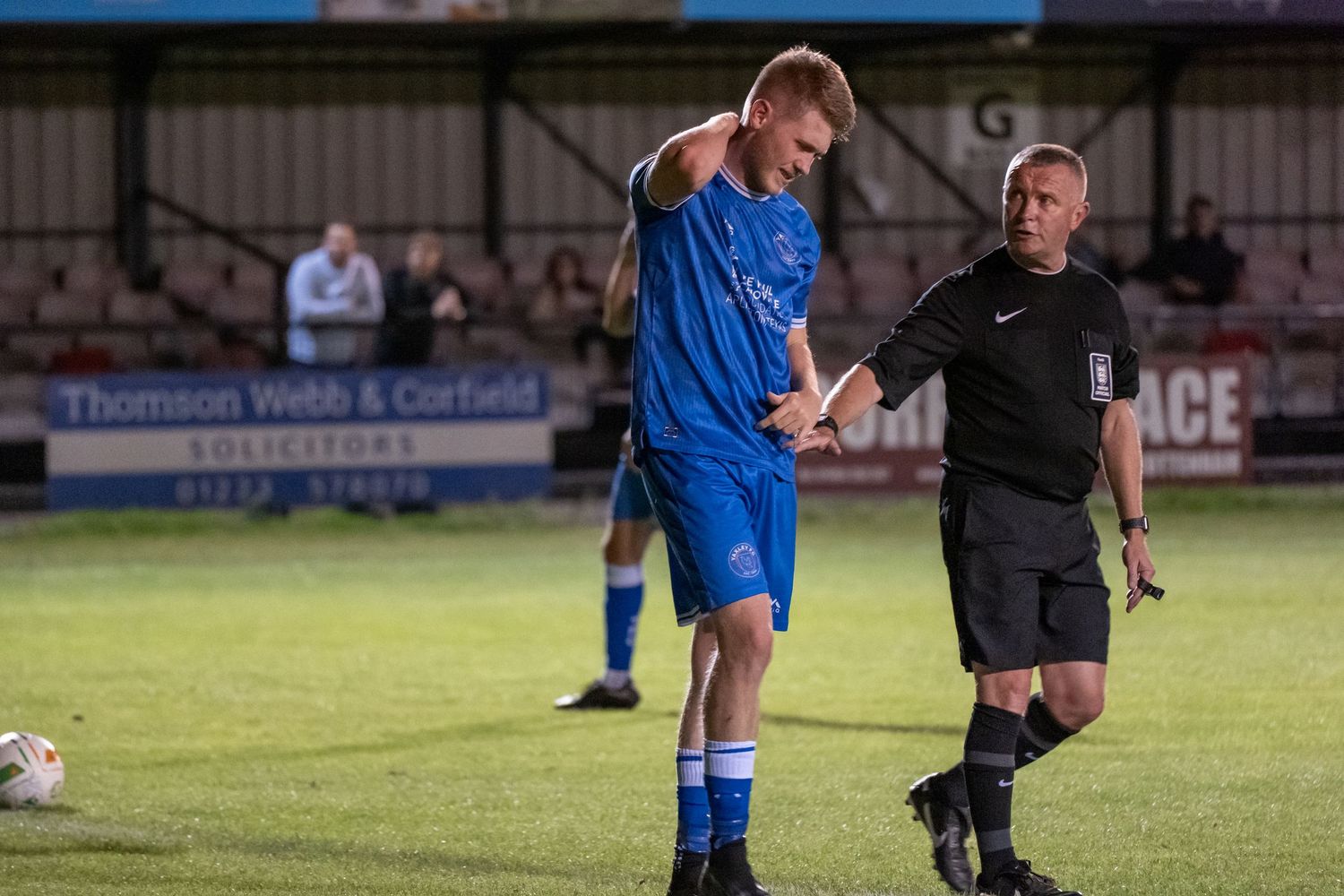 A match official discusses injury with a player during an evening soccer game.