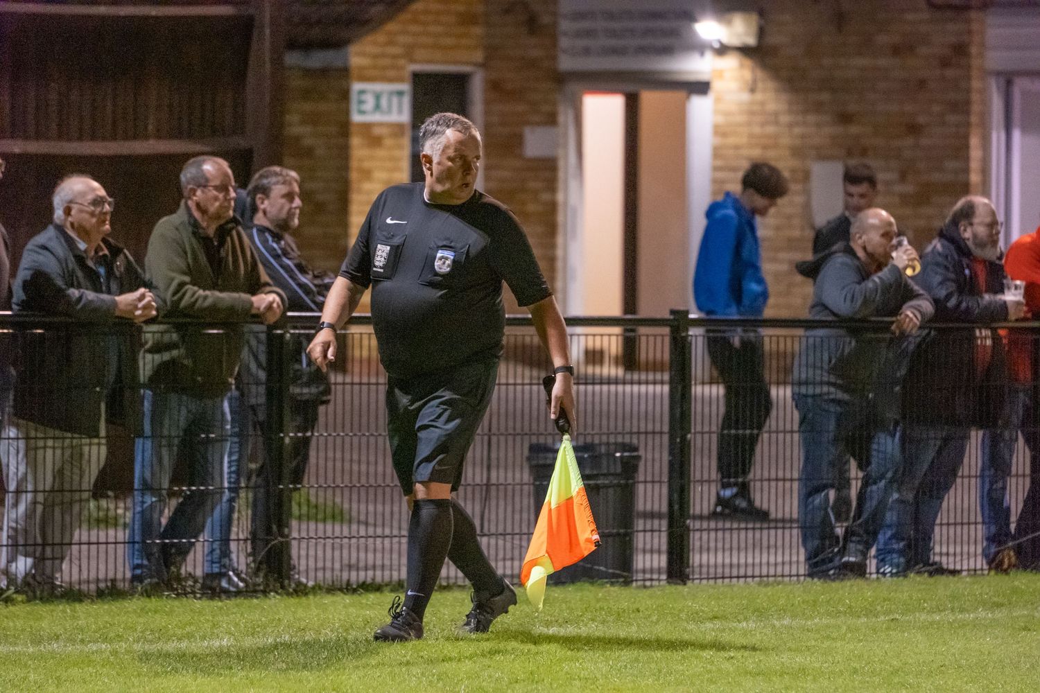 A referee with a flag patrols the sideline during a night match.