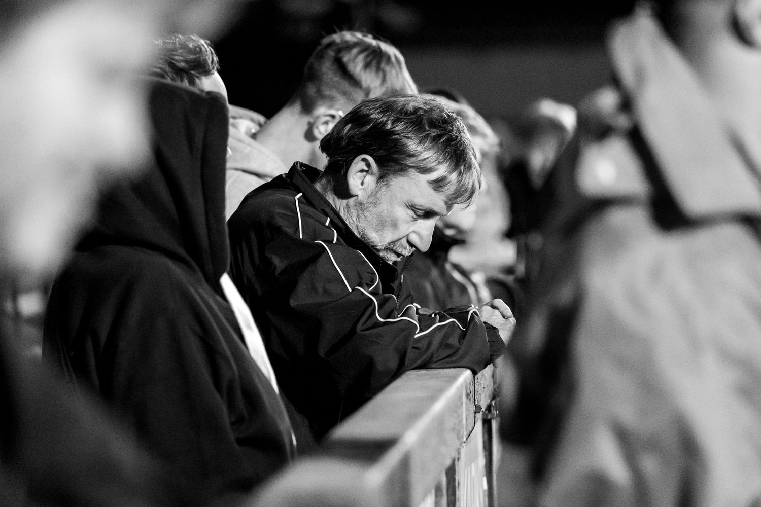 Black and white candid photo of an emotional moment at an football match with spectators in background.