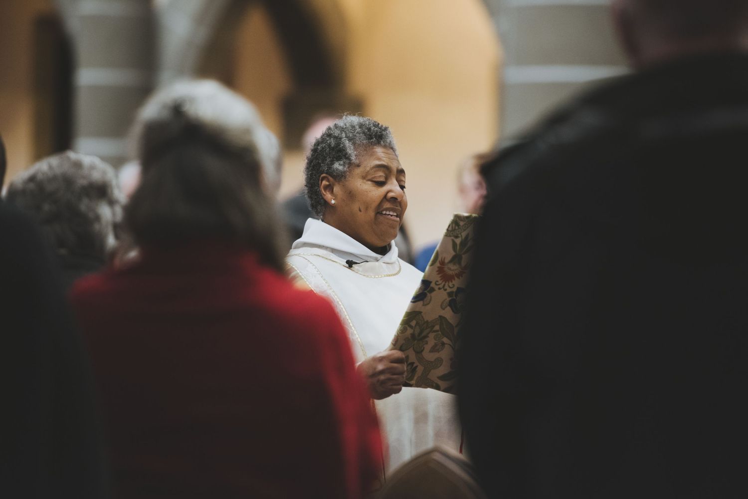 A person in white clothing speaks to a group while others in red attire listen in a church.