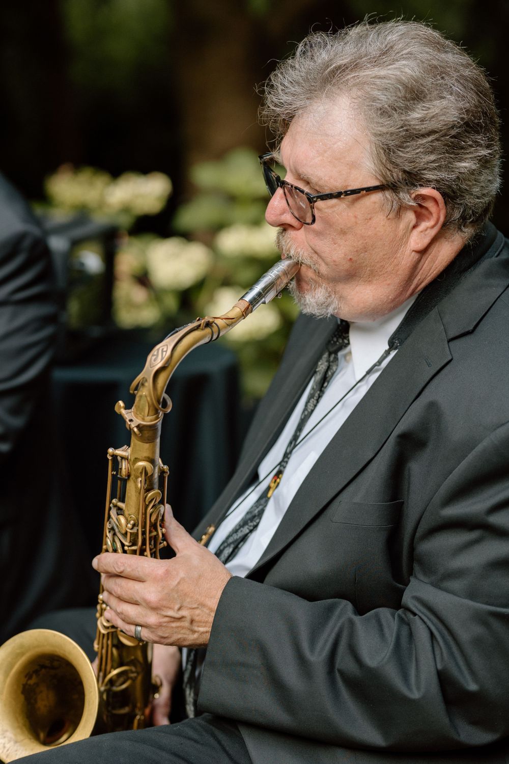 Professional musician in formal attire plays alto saxophone during outdoor performance.