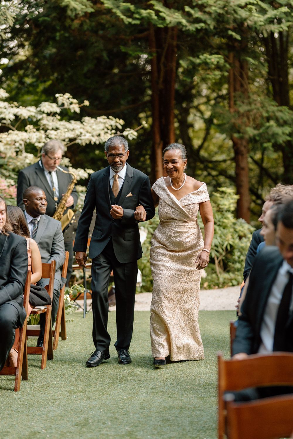 Elegant moment from an outdoor wedding ceremony in a lush garden setting with wooden chairs lining a green aisle.