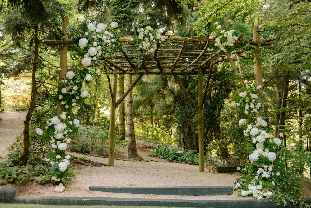 A rustic wooden pergola covered in blooming white roses creates an enchanting garden walkway entrance.