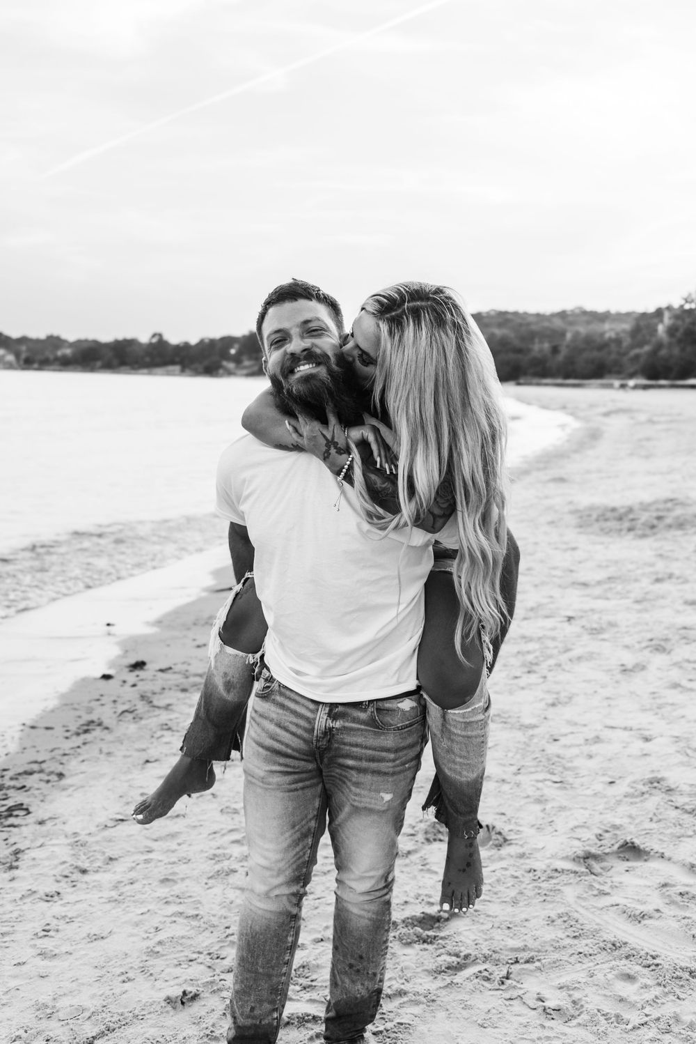 Happy couple in black and white having fun and sharing a playful piggyback ride moment on a beach.