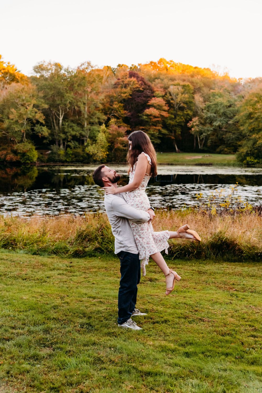 A romantic autumn moment by a lake with vibrant fall foliage in the background during golden hour.