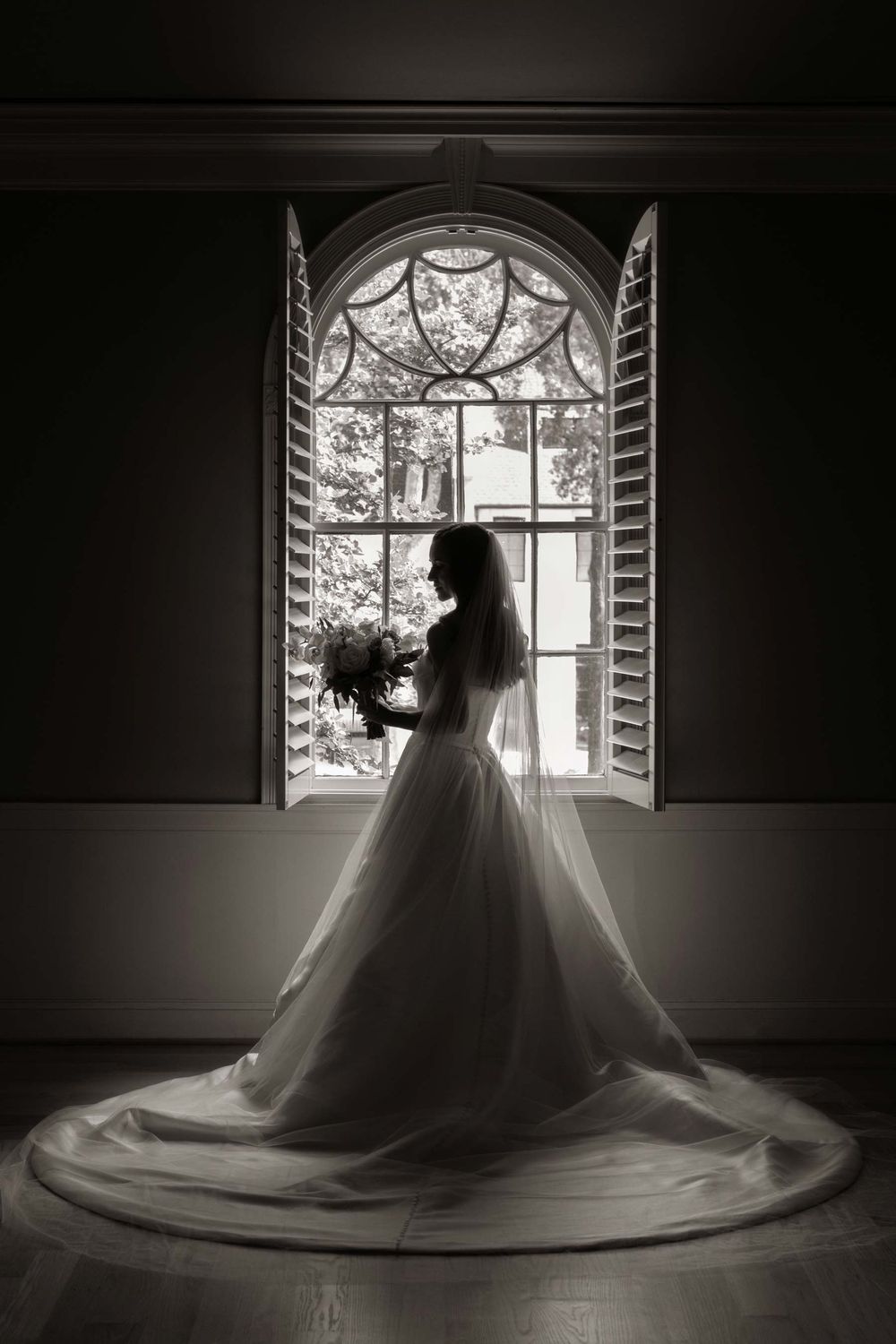 Silhouette of bride by arched window in dramatic black and white photography.