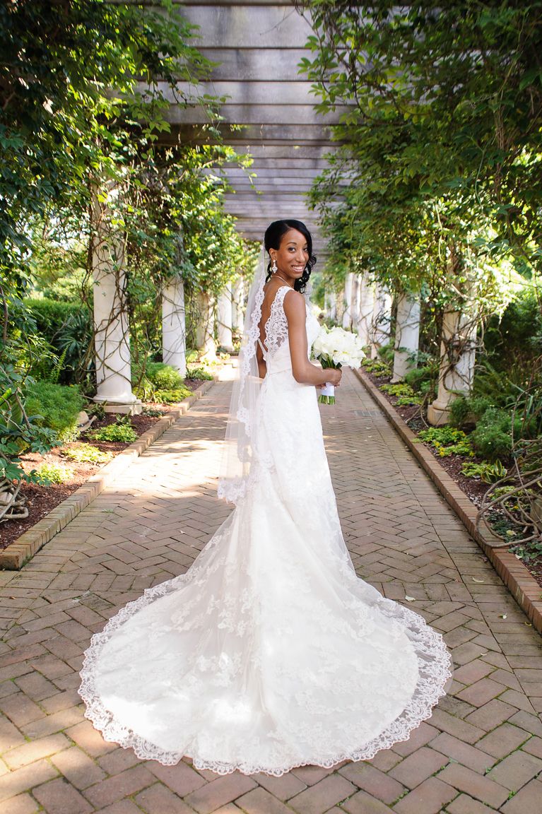 A stunning lace wedding gown with long train photographed in a romantic garden pergola lined with greenery.