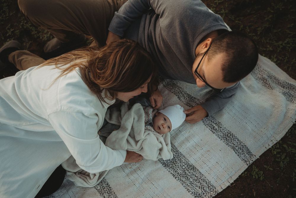 Family shares intimate moment with baby on blanket during outdoor photoshoot.