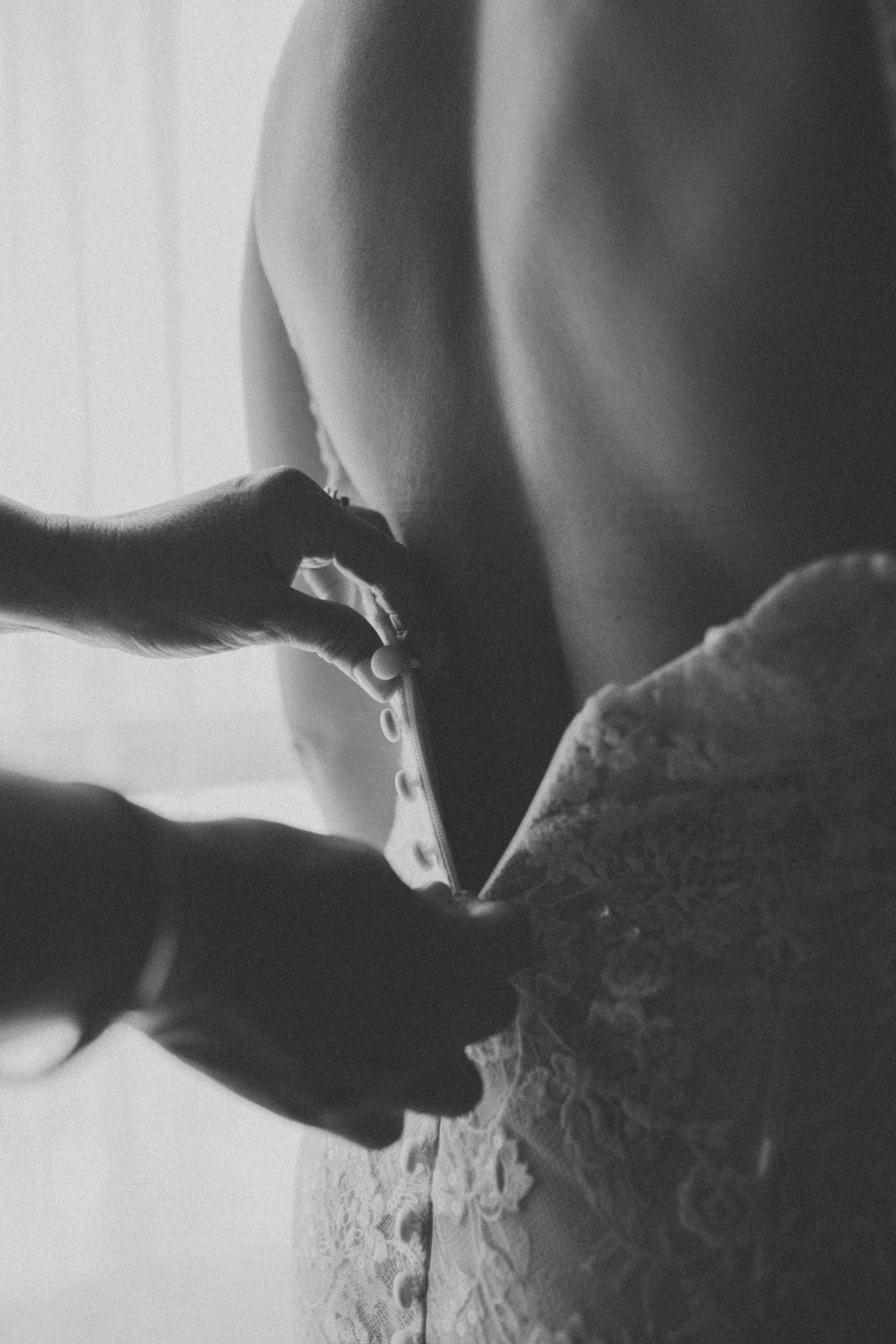 Black and white photograph showing hands fastening or lacing up a corset in dramatic lighting.