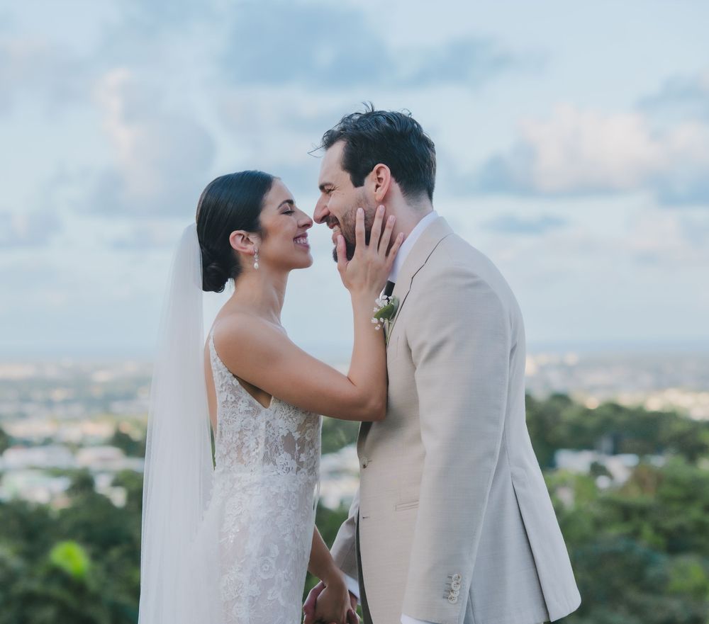 A romantic wedding couple shares an intimate moment on a hilltop overlooking a scenic vista at sunset.