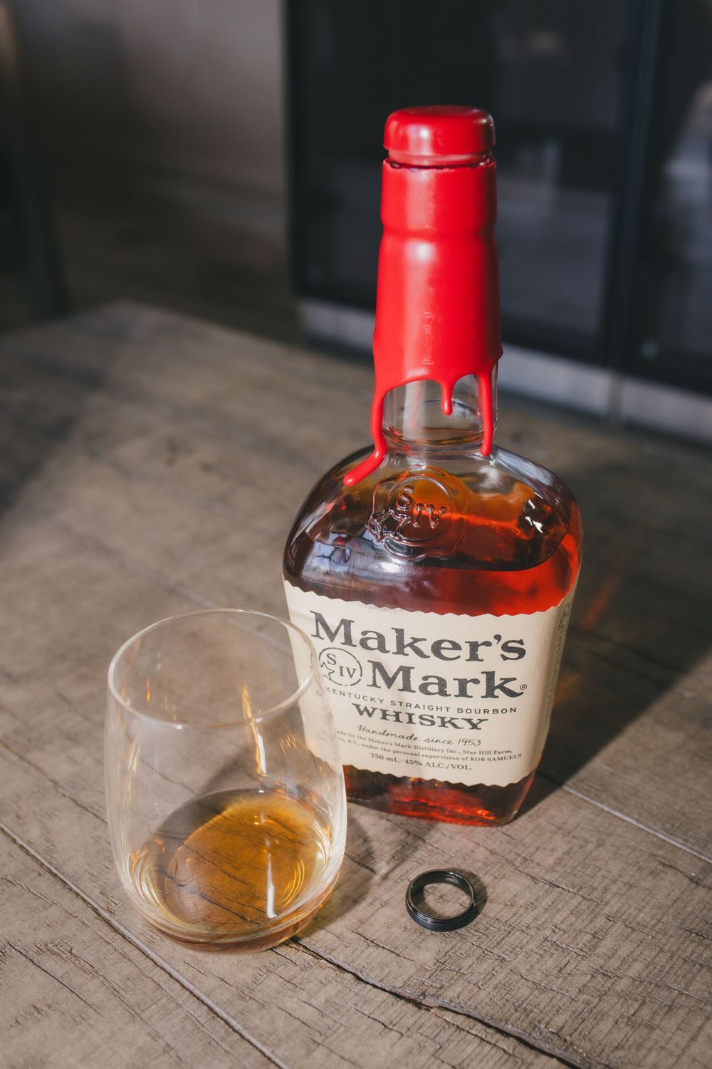 Maker's Mark bourbon whiskey bottle and glass with amber liquid on a wooden surface, shown in progressive pour shots.