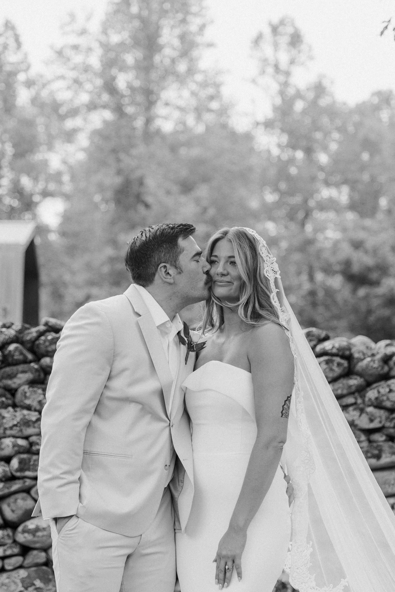 Bride and groom posing together in a line across grass in black and white vintage photograph.