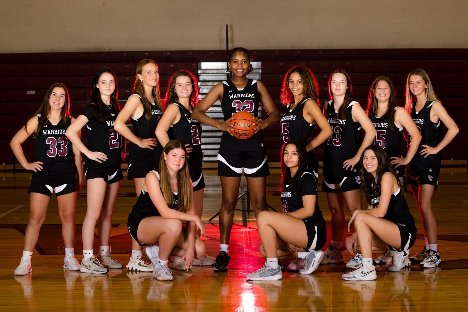 Women's sports team poses in white uniforms under dramatic stadium lighting.