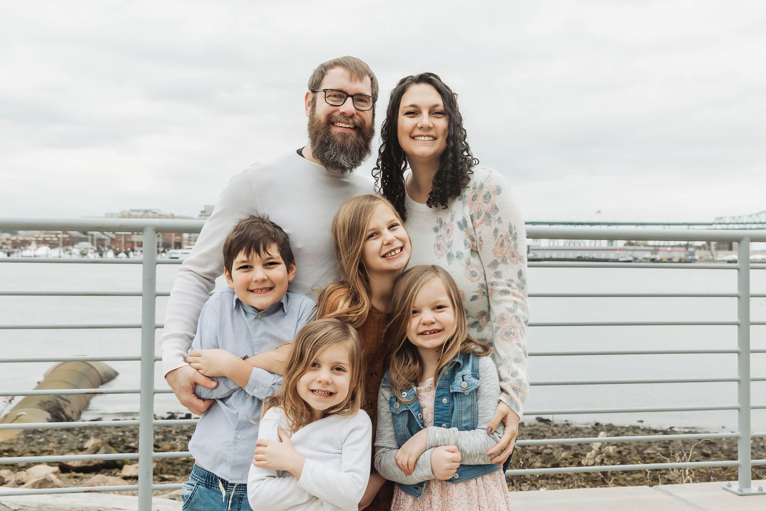 Family of six posing together on waterfront deck with harbor in background.