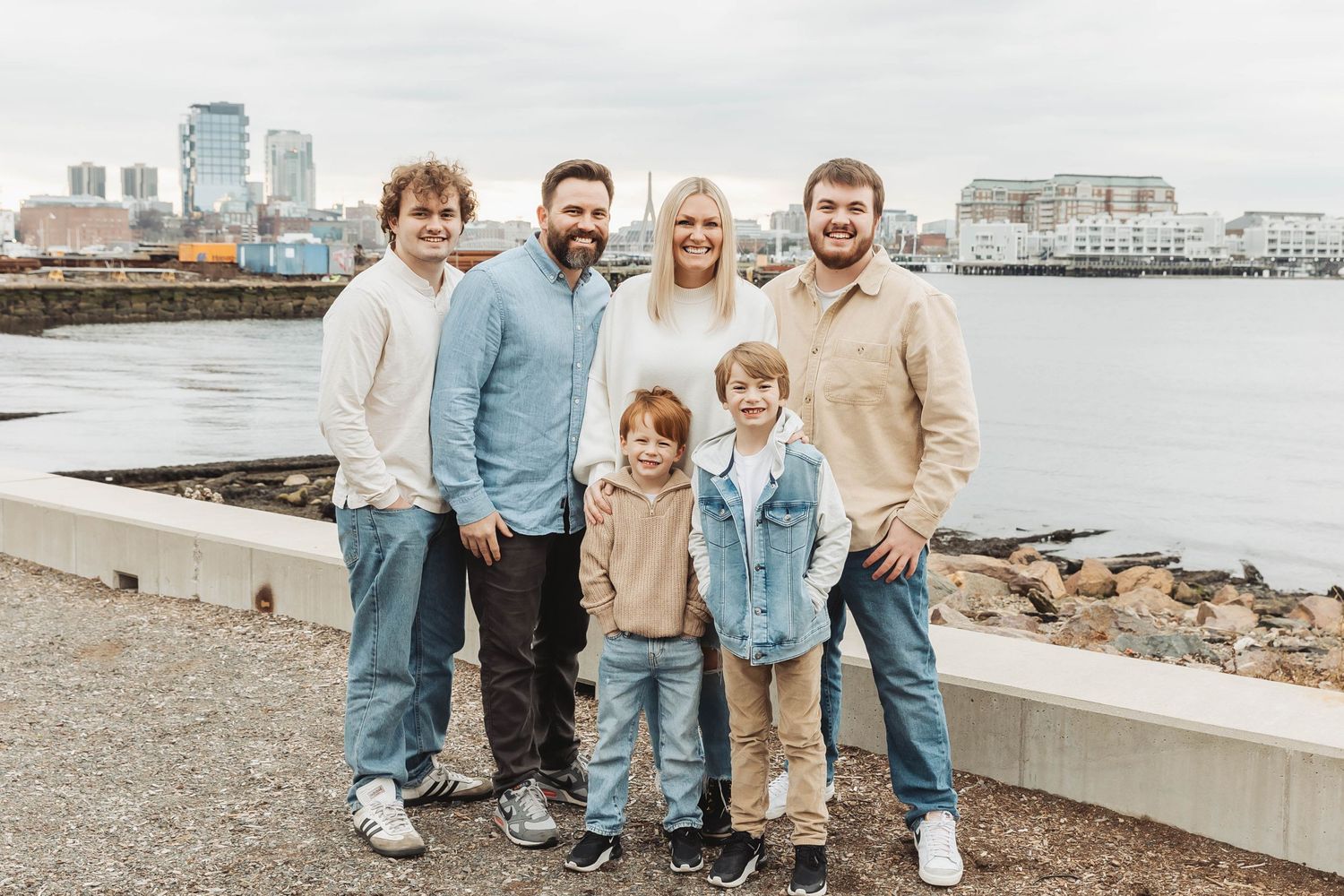 A group poses together by the waterfront on an overcast day with city buildings in the background.