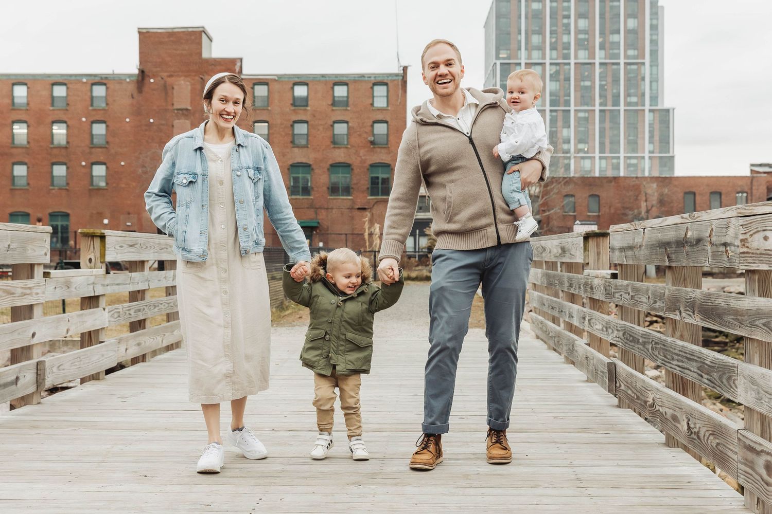 A family walks together on a wooden boardwalk with brick buildings in the background.