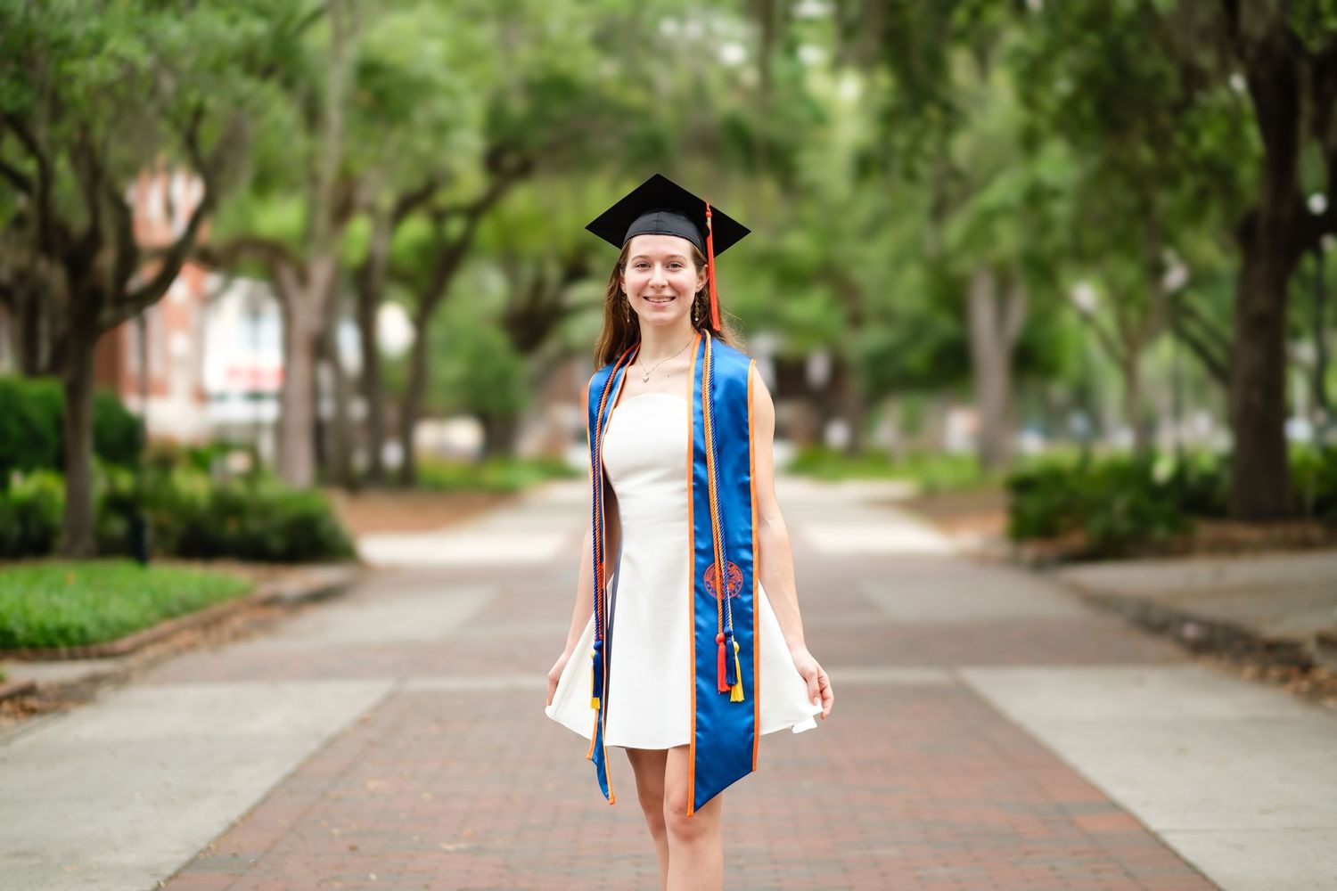 A UF grad wearing a white dress, blue stole and black cap.