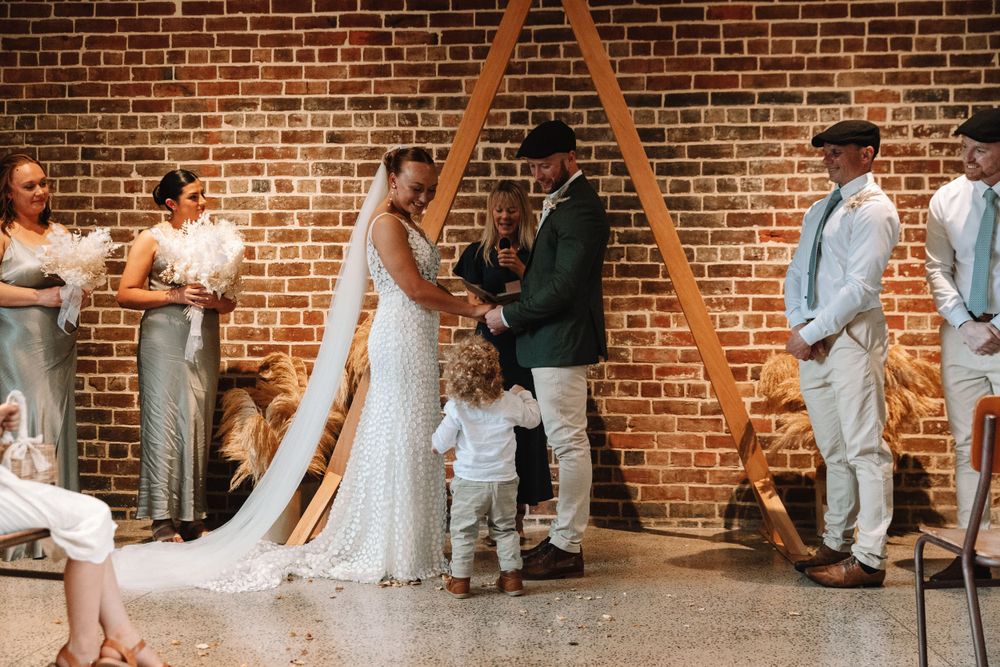 Wedding ceremony under a wooden triangle arch against exposed brick walls.