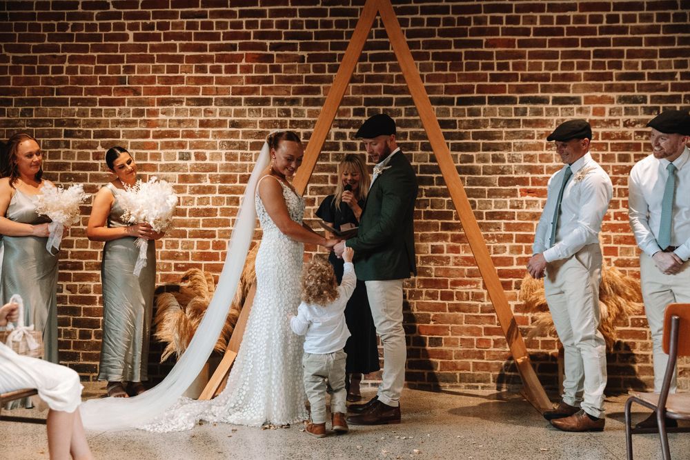 Intimate wedding moment under a wooden triangle arch in an industrial space.
