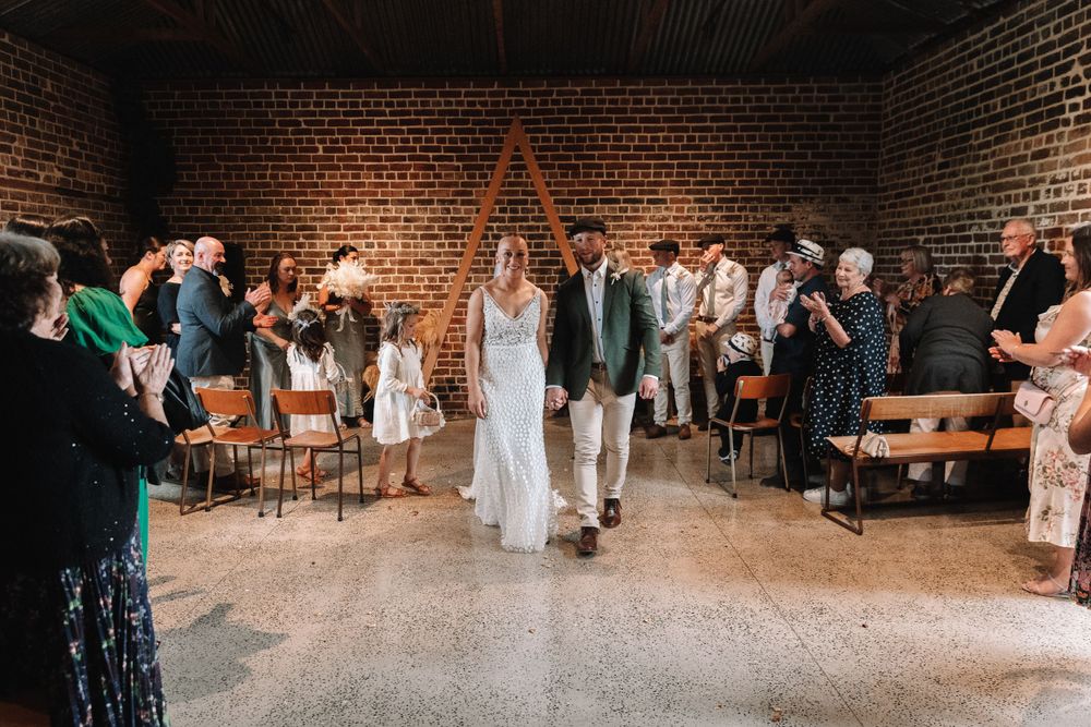 Wedding ceremony in a rustic brick venue with guests seated on wooden chairs.