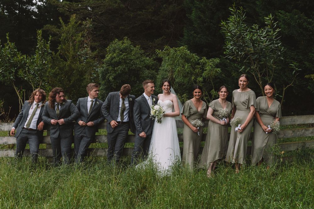 Wedding party poses together in outdoor setting with lush greenery background.