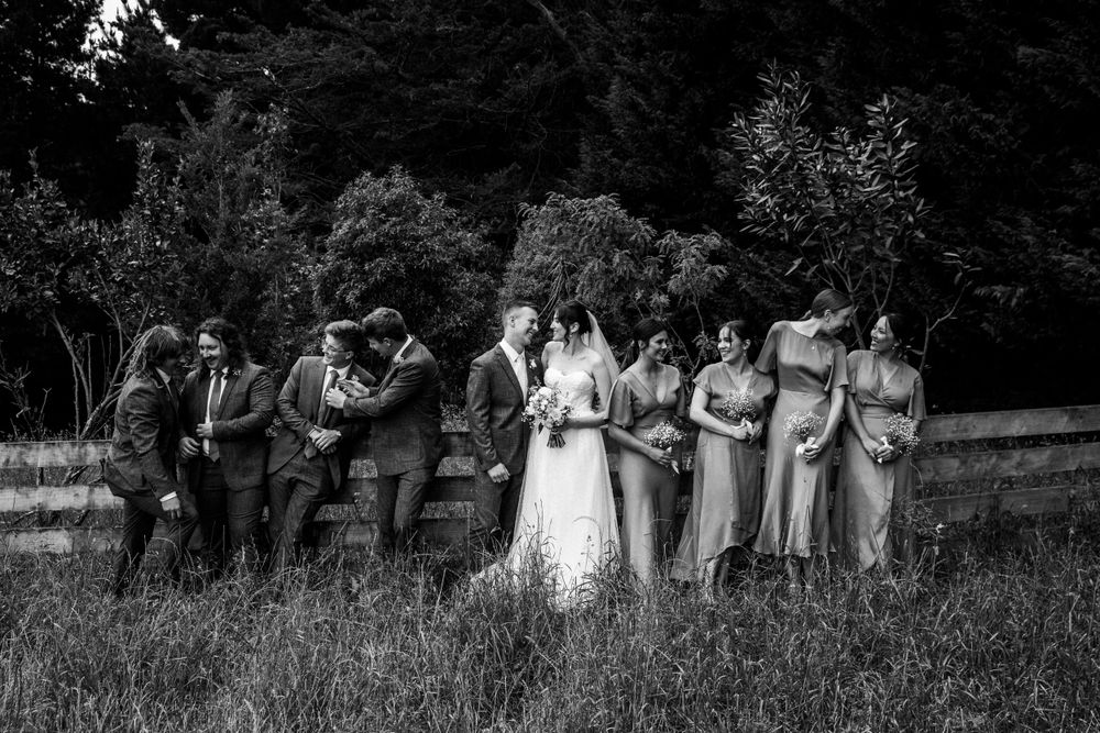 Black and white portrait of wedding party lined up in natural outdoor setting.