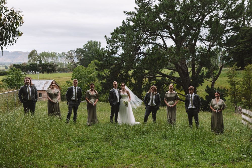 Wedding party lines up in a grassy field with white fence and trees in the background.