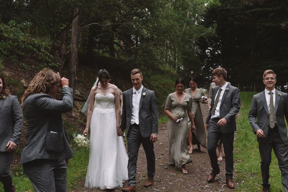 Wedding party gathers on a forest path during a casual outdoor photoshoot.
