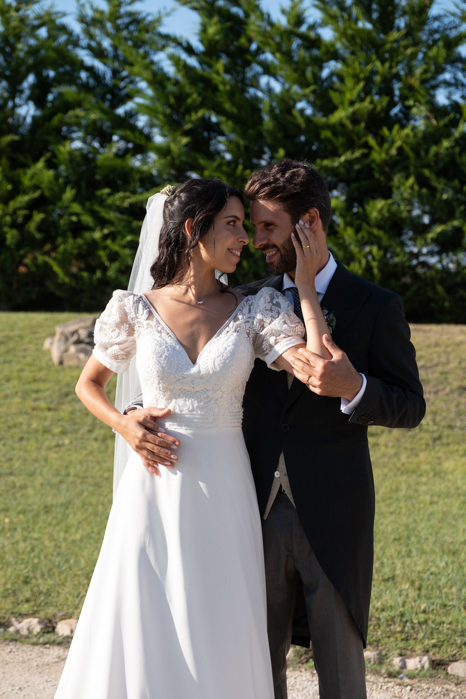 Romantic wedding couple embracing outdoors in front of green hedges on their special day.