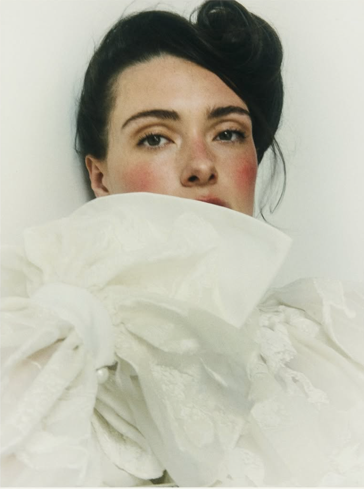 An artistic portrait featuring white fabric draped dramatically against a light background.