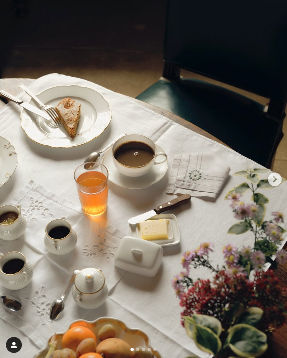 An elegant breakfast table setting with coffee, juice, and flowers on a white tablecloth.