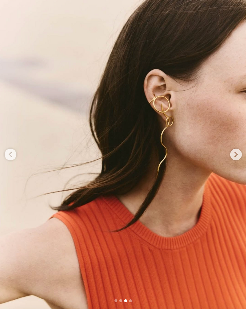 Close-up of gold sculptural earring worn with orange ribbed sleeveless top.
