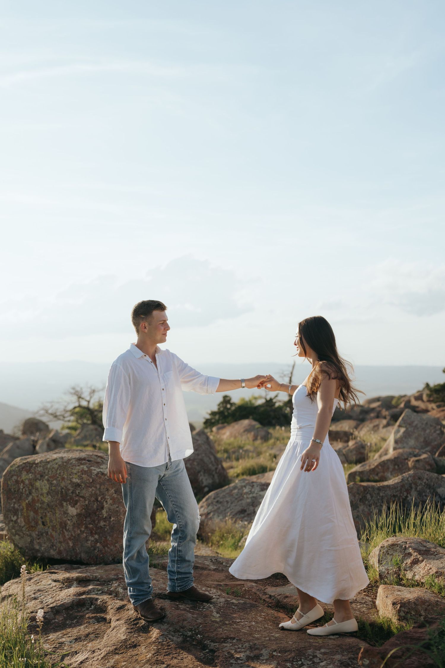 Couple in white and casual attire poses on rocky terrain during Oklahoma sunset.