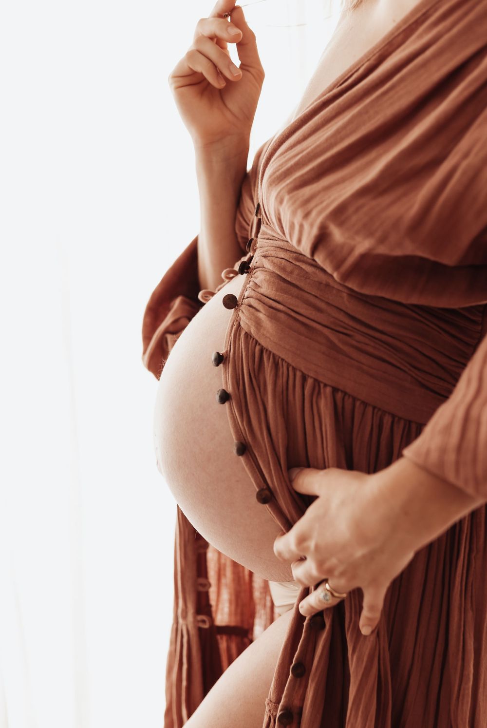 Close-up view of a pregnant belly in a rust-colored dress with button details against a light background.