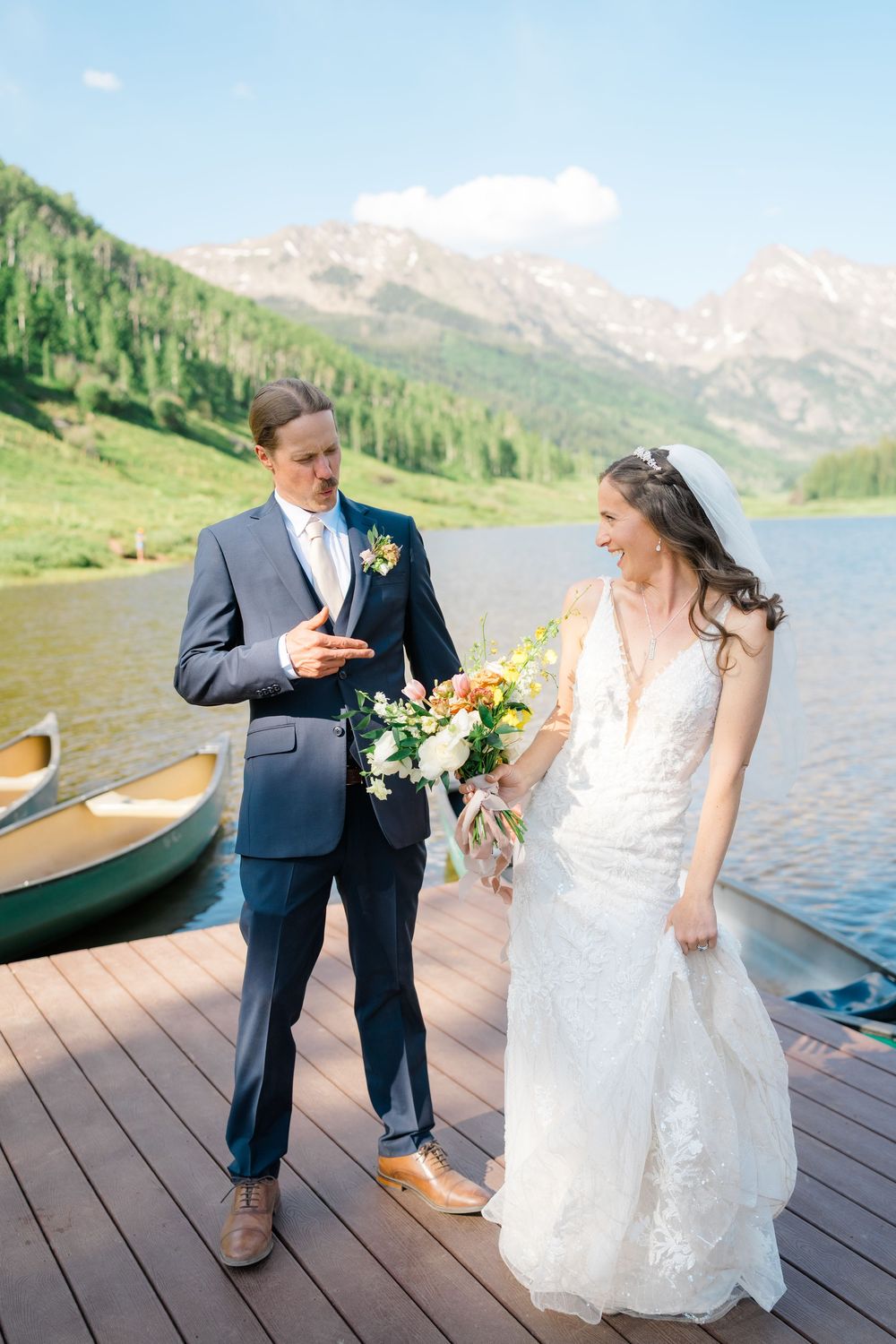 husband and wife laugh together in front of lake as he makes hand guns at her