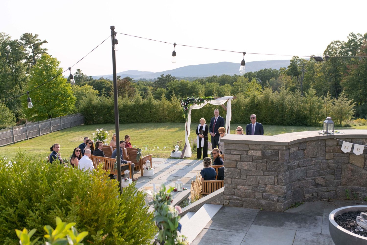 Outdoor wedding ceremony setup with string lights and stone walls overlooking scenic mountain landscape.