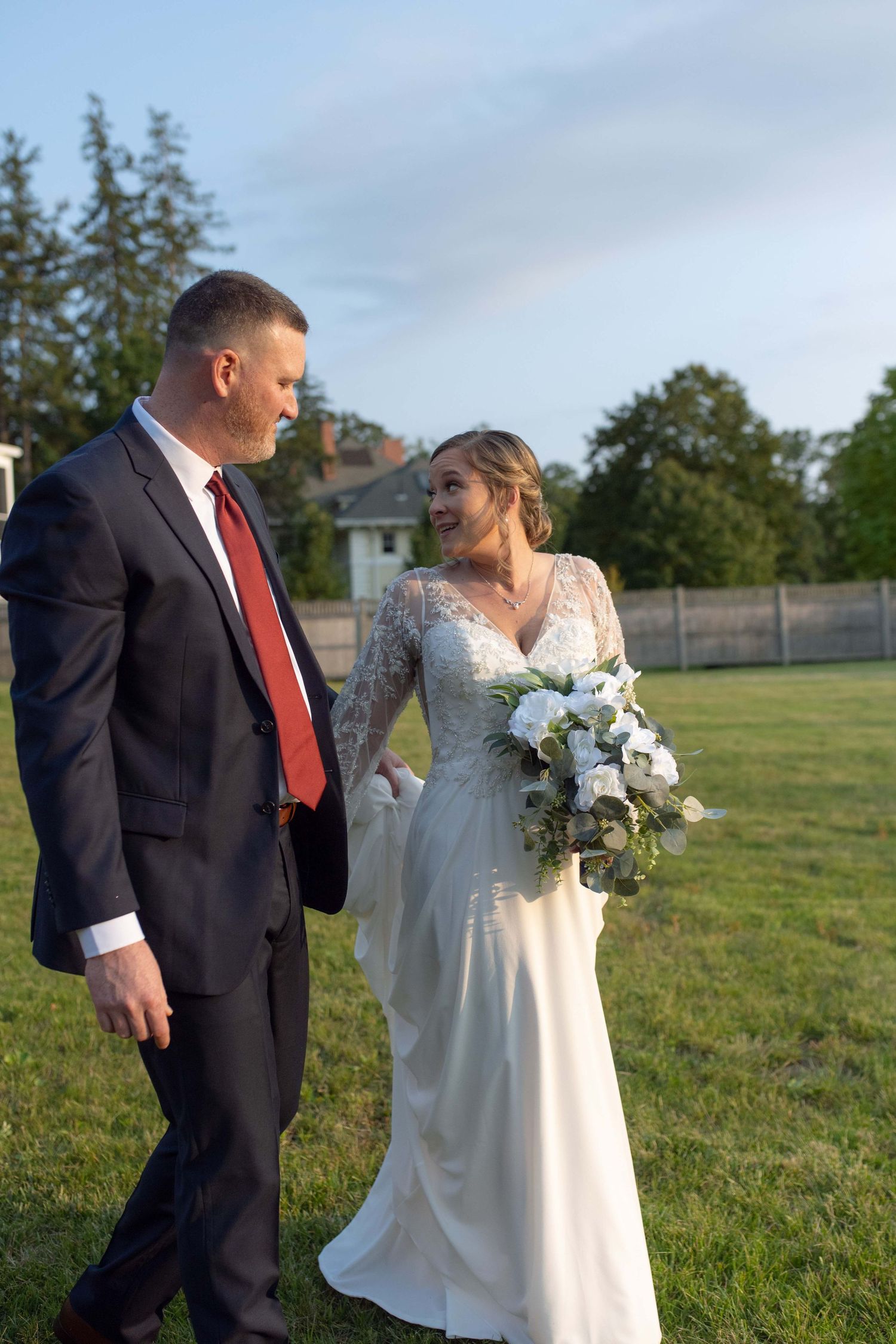 A couple in wedding attire share a moment outdoors with the bride holding a blue and white bouquet.