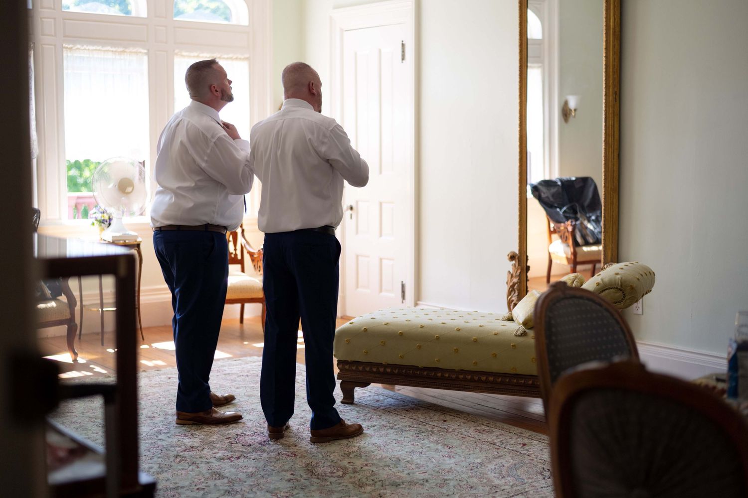 Two people in white dress shirts stand in conversation near a doorway of a bright interior room.