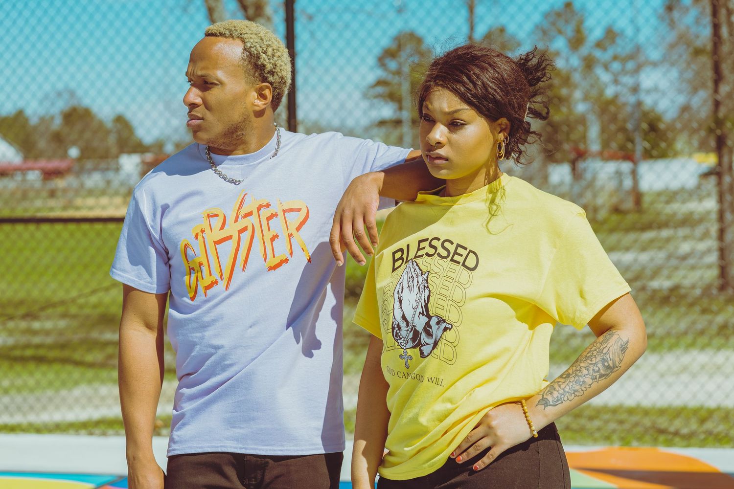 Two people wearing casual t-shirts standing together outdoors on a sunny day.