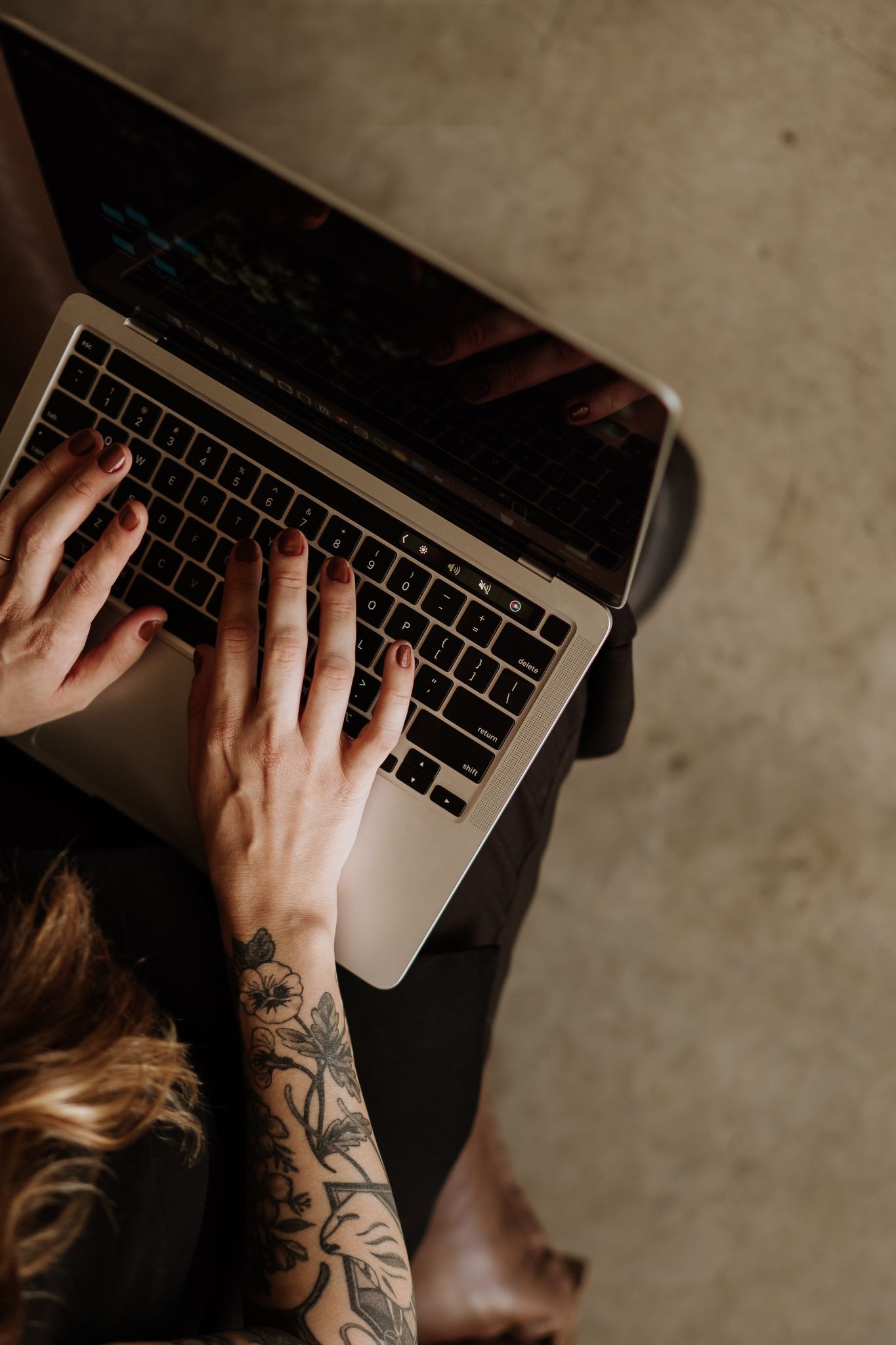 Overhead view of tattooed hands typing on MacBook laptop keyboard.