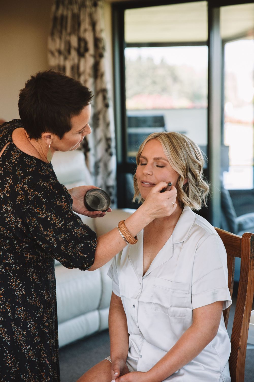 A makeup artist applying cosmetics during wedding preparations in a sunlit room.