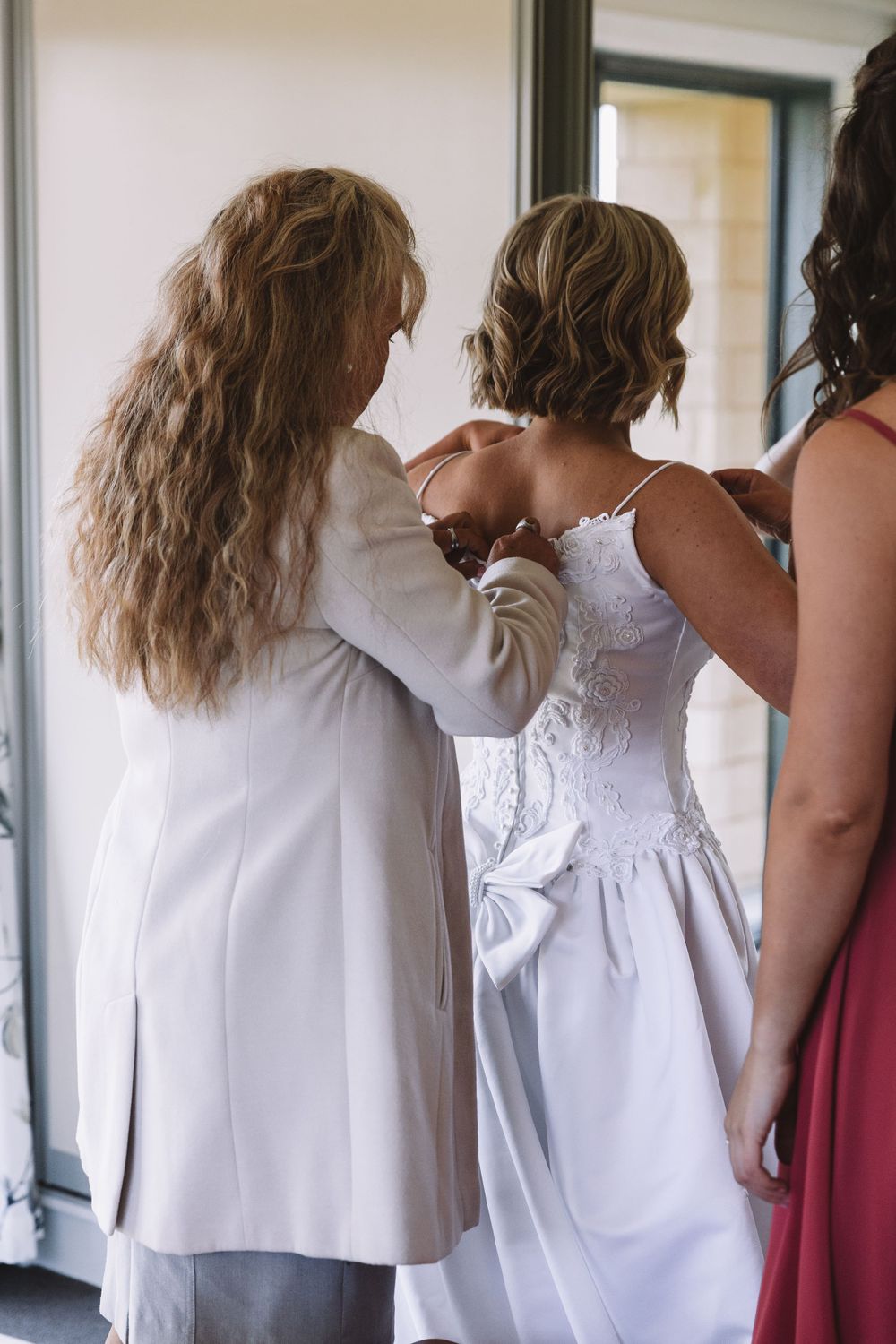 Helpers assisting with the back of a white wedding dress.