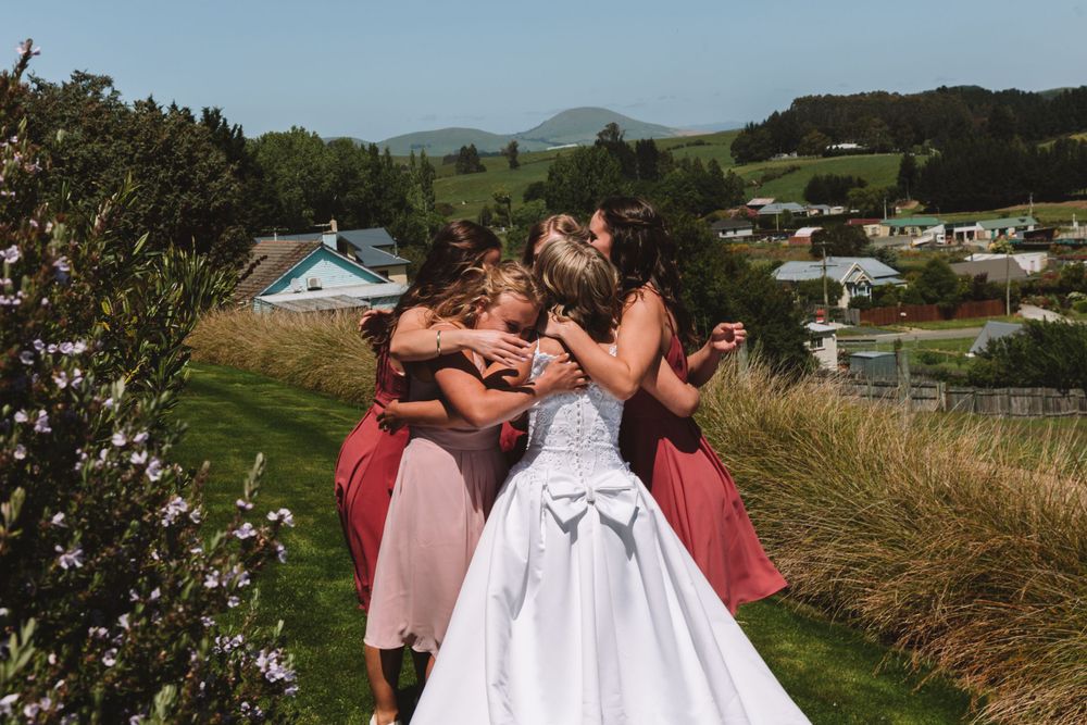 A group embraces in a joyful moment during a wedding on a grassy hilltop.